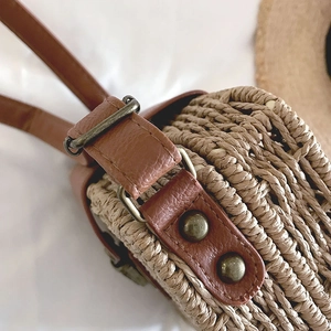 Close-up of woven straw texture with brown leather trim and retro hardware details