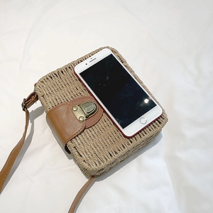 Detail of straw woven crossbody bag with brown leather flap next to a smartphone for scale