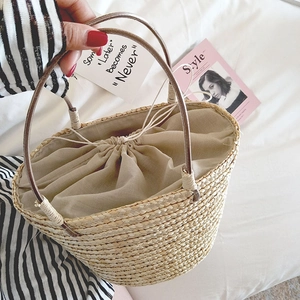 Detail view of woven straw bucket bag with beige drawstring lining and leather handles