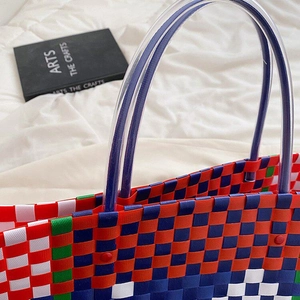 Close-up of woven plastic tote bag with colorful plaid pattern and red rivet detail