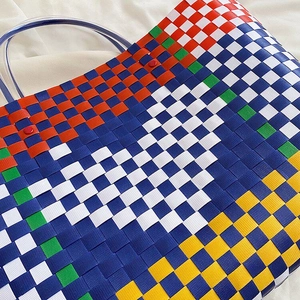 Close-up of a colorful woven plastic handbag with geometric pattern and clear handles