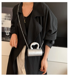 Sac de soirée cylindrique argenté avec poignée en métal et chaîne porté par un mannequin