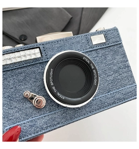 Détail du sac caméra en denim bleu avec coutures blanches et finitions en strass brillants