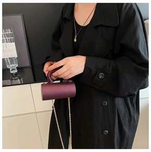 Vue détaillée du mini sac cylindrique bordeaux avec chaîne dorée sur un manteau noir