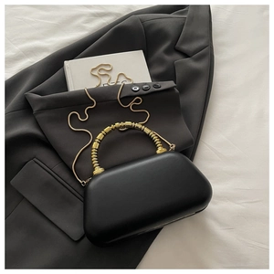 Detail of black matte hard-shell evening bag with gold beaded handle and chain