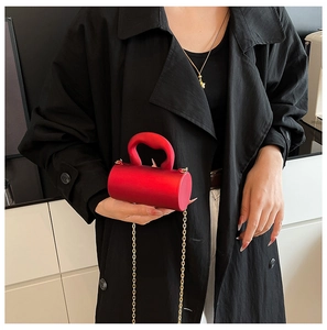 Détail d'un sac à main cylindrique rouge en velours avec anse épaisse et chaîne dorée