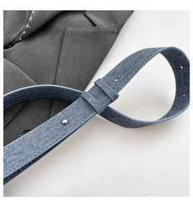 Détail de la ceinture bleu denim avec boucle argentée sur une veste grise