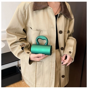 Mini sac cylindrique vert émeraude avec chaîne dorée porté sur une veste kaki