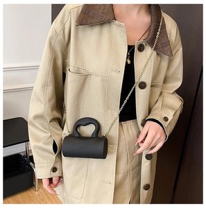 Détail d'un mini sac cylindrique noir avec poignée en acrylique et chaîne dorée
