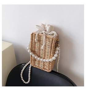 Detail of woven straw bucket bag featuring pearl shoulder strap and canvas drawstring liner