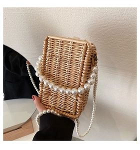 Detail of woven straw handbag featuring elegant pearl chains and linen drawstring lining