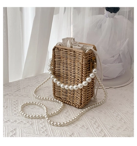 Detail of hand-woven straw crossbody bag with elegant pearl strap and drawstring lining