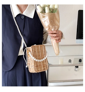 Detail of woven straw crossbody bag with elegant pearl strap and drawstring closure