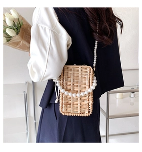 Detailed view of woven straw crossbody bag featuring pearl strap and drawstring closure