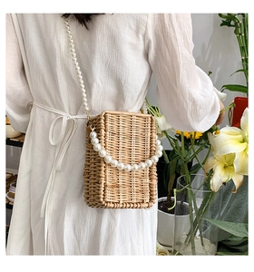 Detail of woven straw box bag with decorative white faux pearl strap on model