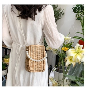 Detail of woven straw box bag with premium pearl crossbody chain and handle texture