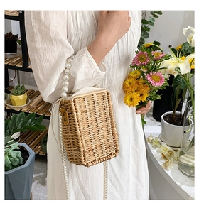 Detail of woven straw bucket bag with elegant pearl handles and drawstring inner lining