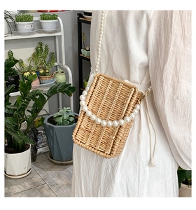 Detail of woven straw square bag with pearl handle and drawstring lining on model