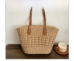 Détail du sac cabas en paille tressée évidée avec anses en cuir marron sur table