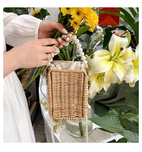Detail of hand-woven straw bag featuring pearl handle and secure drawstring liner