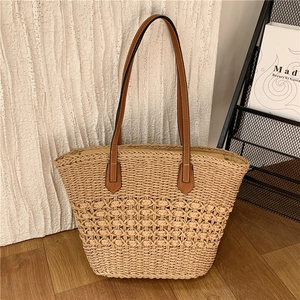 Détail du grand sac cabas en paille avec des anses en cuir marron sur fond minimaliste