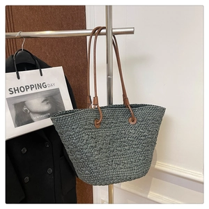 Detail of dark green woven tote bag with brown leather straps on a hanger