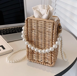 Handwoven rattan crossbody bag with pearl chain strap and drawstring lining on a desk