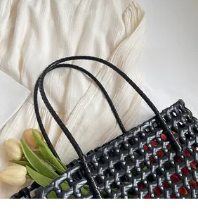 Detailed top view of black woven tote bag with smooth long handles on white fabric