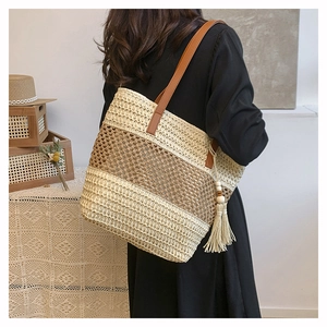Detail of woven straw tote bag with brown leather straps and beige tassels on a model