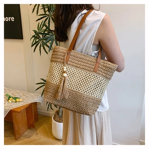 Detail of woven straw tote bag with color-block stripes and tassel charm on shoulder strap