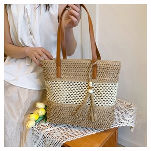 Detail of straw woven tote bag with contrast stripes and bohemian tassel ornament