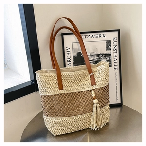 Detail of two-tone woven straw tote bag with brown leather straps and wooden bead tassel