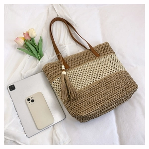Detail of straw woven tote with brown leather handles and decorative tassel and wood beads