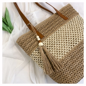 Detail of striped straw tote with leather handles and bohemian tassel on white fabric