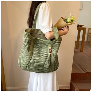 Detail of green crochet straw tote bag with wood bead tassels and hollow woven pattern