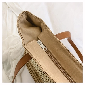 Detail of straw tote bag showing smooth zipper closure and woven plant fiber texture