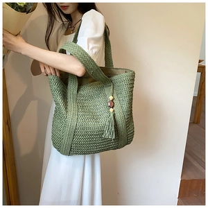Detail of hand-woven straw tote in green with wooden bead tassels for summer vacation