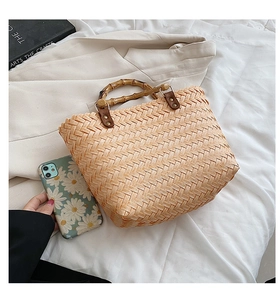 Detail of handwoven handbag featuring natural bamboo handles and textured straw material