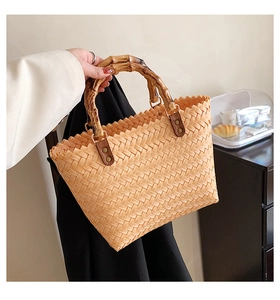 Detail of woven light orange handbag with bamboo-style handle and rivet accents