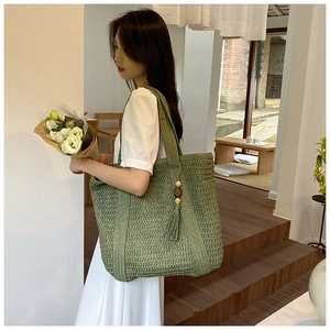 Detail of green woven straw tote bag with elegant tassel and wooden beads decoration