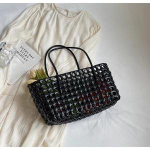 Detail of black handwoven tote bag featuring intricate diamond weave and slim dual handles