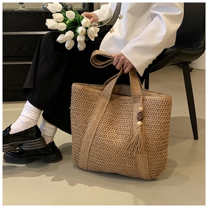 Close-up of woven straw tote bag with long tassel pendant and wooden bead detail