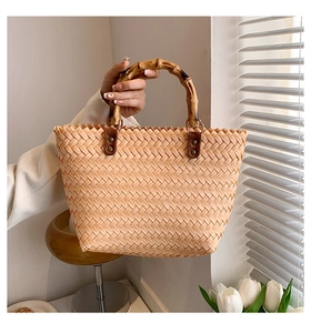 Detail of woven handbag featuring natural bamboo handles and textured herringbone pattern