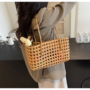 Detail of hand-woven hollow straw tote bag with long handles shown on model's shoulder