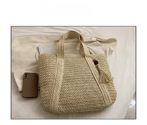 Detailed view of beige woven straw tote bag with fringe charm and phone for size reference