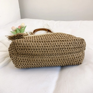 Handwoven straw beach bag with brown leather handles and decorative tassel on white fabric