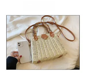 Straw handbag with bamboo handle and leather strap shown next to phone for size reference