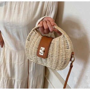Detailed close-up of straw woven bag showing leather strap and metal twist-lock buckle