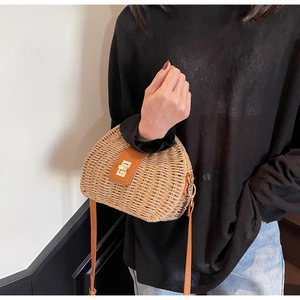 Detailed view of straw woven bag with leather flap and golden twist lock on model