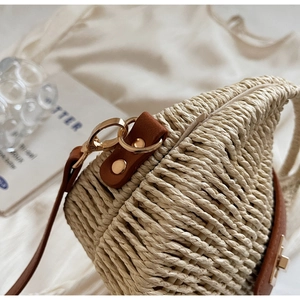 Detail of hand-woven straw bag featuring brown leather strap and golden metal hardware